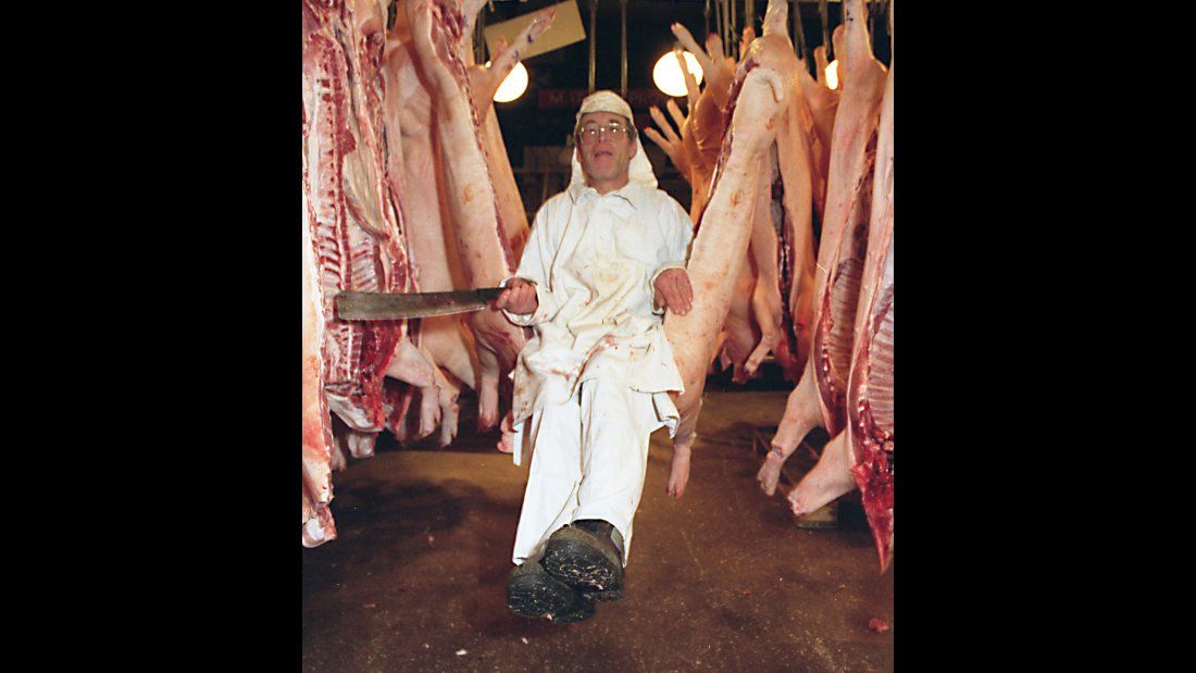 slaughterhouse worker using a hanging pig carcass as a swing