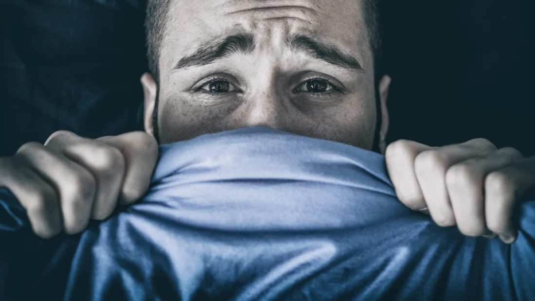 scared man hiding under duvet